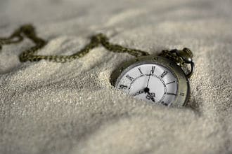 This shows a pocket watch resting on sand. Image is from the How Long To Let Wood Glue Dry Before Sanding blog article.