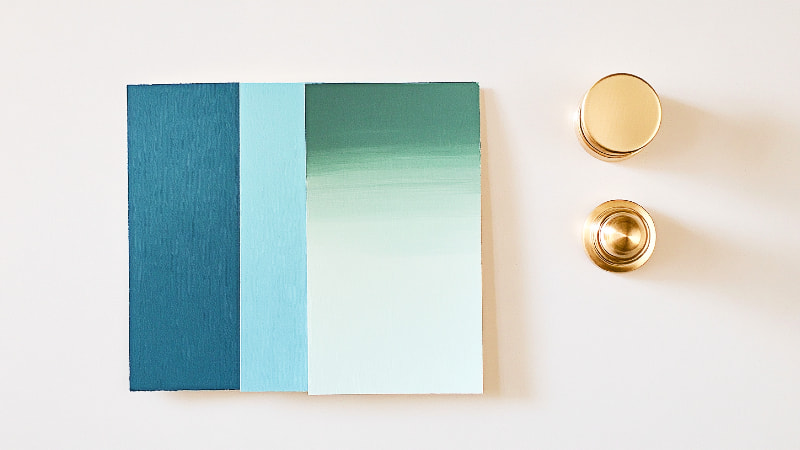 A flat lay of planning materials for a cupboard makeover, including deep green and blue paint color swatches and elegant brass hardware samples.