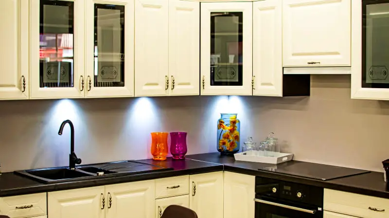 A stylish kitchen with warm off-white cabinets and a black countertop, accented by an orange vase and a purple vase.