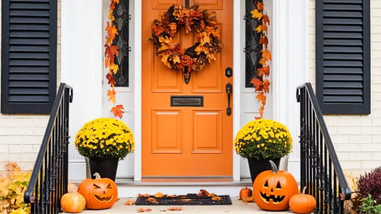 A warmly lit front door adorned with a smiling jack-o'-lantern, colorful fall foliage, and a decorative Halloween wreath.