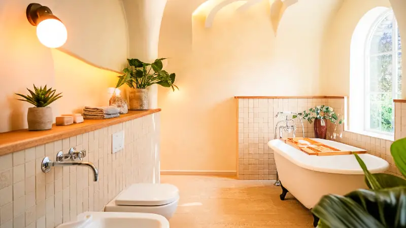 A bright, inviting bathroom interior with a mix of modern and cozy elements, featuring warm natural light, soft textures, and a subtle touch of greenery. The space is spacious and aspirational.
