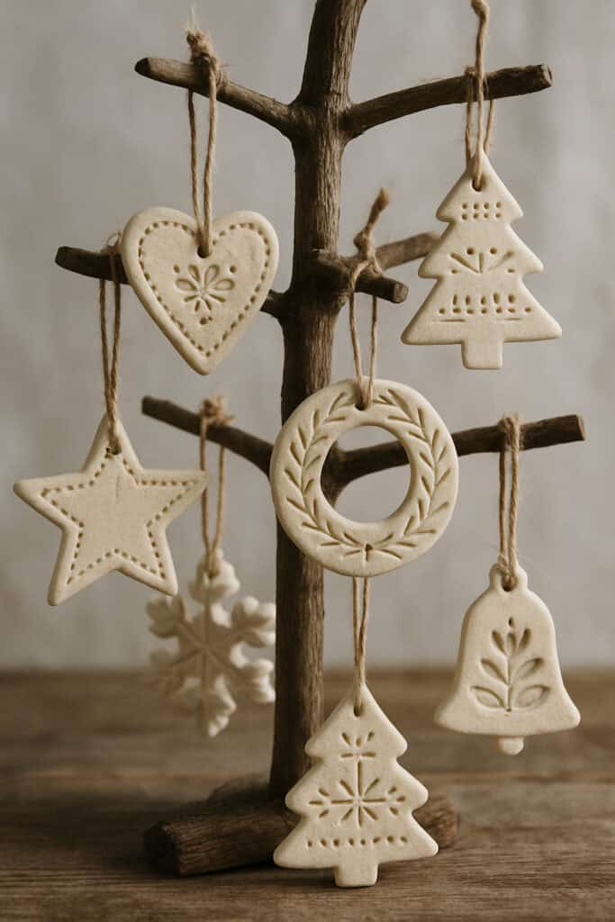 A collection of Scandinavian-inspired salt dough ornaments hanging from a wooden tree, featuring various shapes like hearts, stars, and Christmas trees.